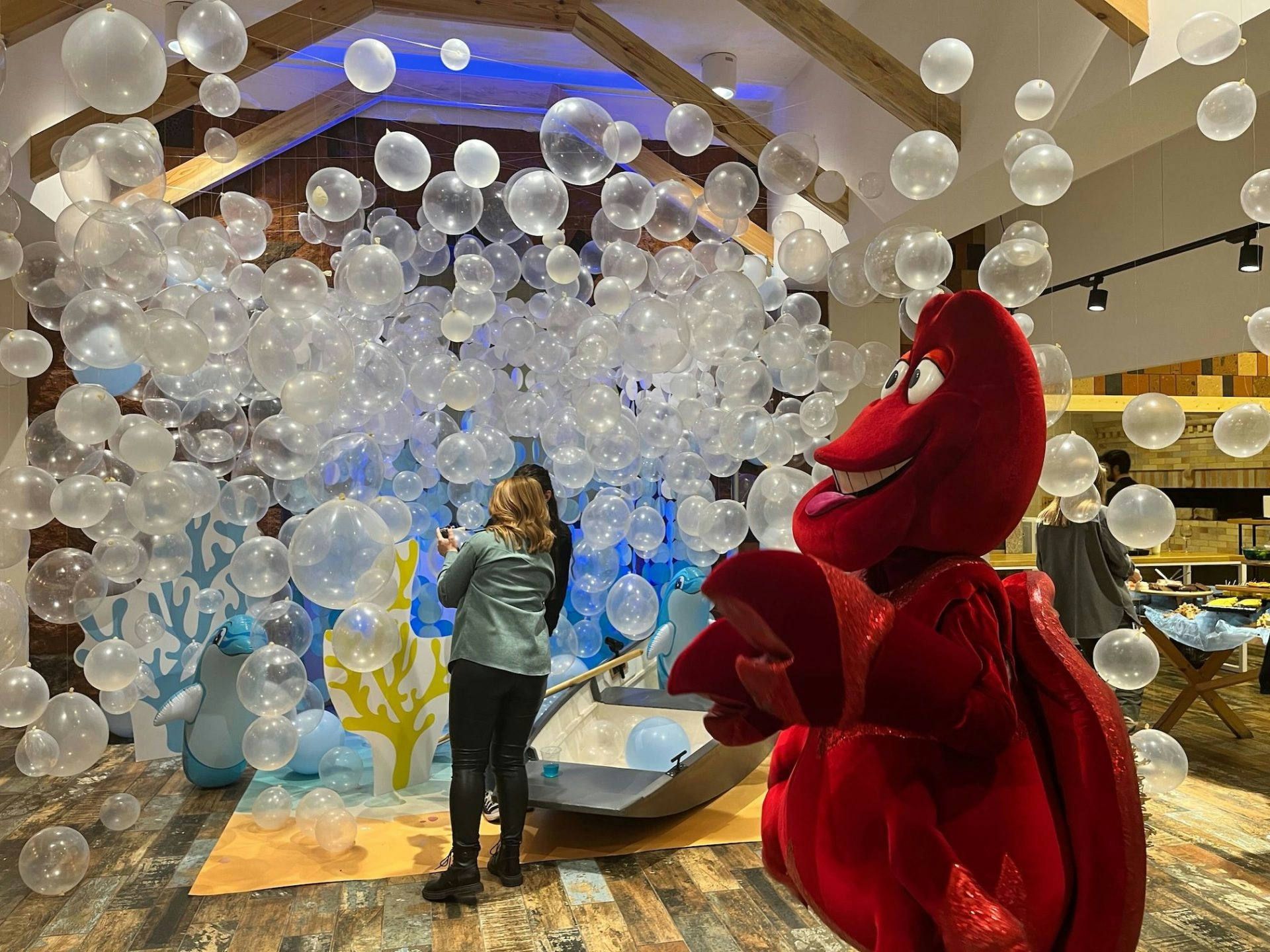 At a Miro office party, balloons float through the air like bubbles and a person dressed in a crab suit wades through the bubbles.